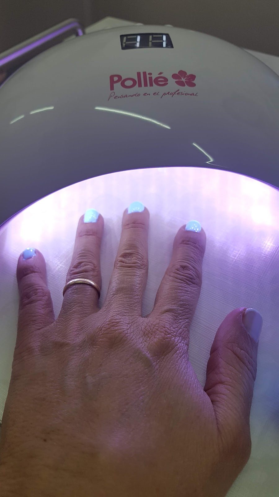 Manicura semipermanente en azul claro secándose bajo la lámpara de uñas